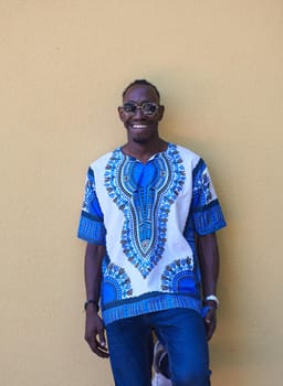 Close up portrait of a smiling young african man wearing traditioinal clothes standing isolated over yellow wall background