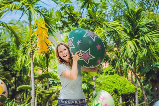 Beautiful young woman with bunny ears having fun with traditional Easter eggs hunt, outdoors. Celebrating Easter holiday.