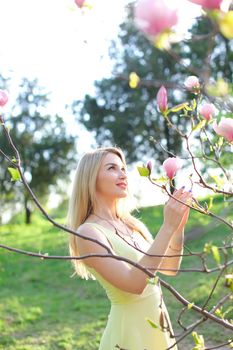 Young blonde girl standing near magnolia in park. Concept of spring seasonal and nature.