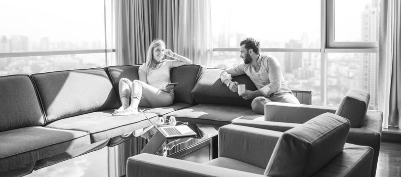 Young couple relaxing at  home using tablet computer reading in the living room near the window on the sofa couch.