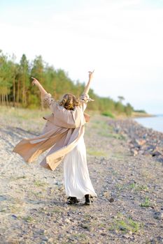 Young girl turning around with raising forefingers up on sea beach. Concept of summer vacations and enjoying freedom.