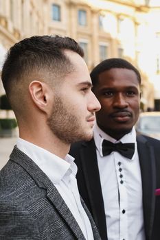 close up portrait of same sex couple. caucasian man wearing suit standing near afro american boy. Concept of business and male fashion.