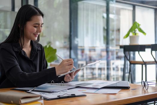 Attractive businesswoman using a digital tablet while working with paperwork financial data chart.