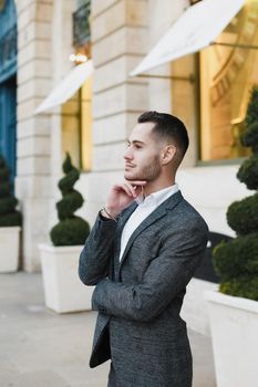 Young cacuasian male person wearing suit standing near building outdoors. Concept of fashion and businessman, urban life.