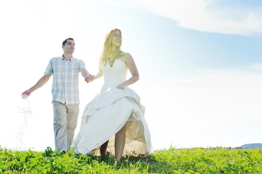 happy bride and groom walking and run on beautiful meadow outdoor at sunset