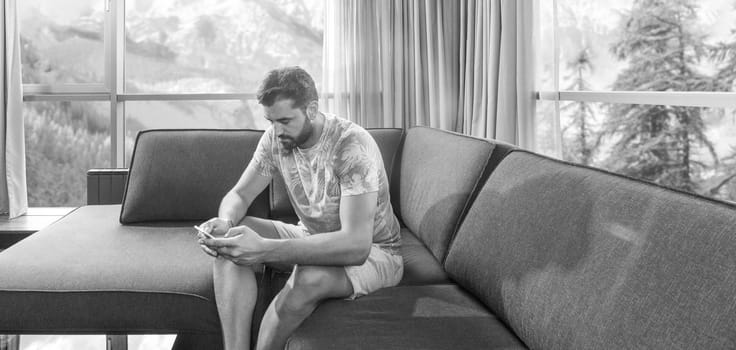 young man sitting on sofa and using a mobile phone  near the window at home