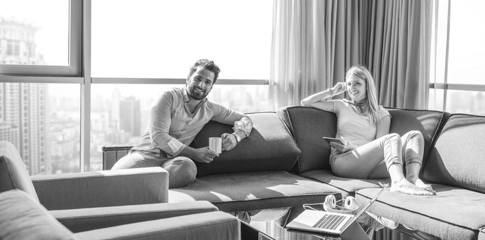 Young couple relaxing at  home using tablet computer reading in the living room near the window on the sofa couch.