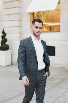 Young cacuasian male person wearing suit standing near building outdoors. Concept of fashion and businessman, urban life.