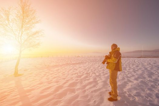 portrait of young cheerful male photographer while taking photographs of sunset or sunrise with digital camera at winter mountains  Young man shooting photos outdoors