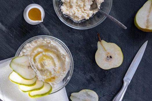 cottage cheese poured with syrup with slices of fresh pear, dark background, top view