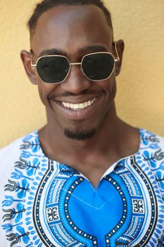 Close up portrait of a smiling young african man wearing traditioinal clothes standing isolated over yellow wall background