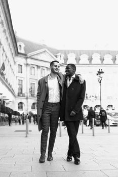 Black and white bw portrait in Paris. Caucasian man running with afroamerican male person and holding hands in city. Concept of happy gays and strolling.