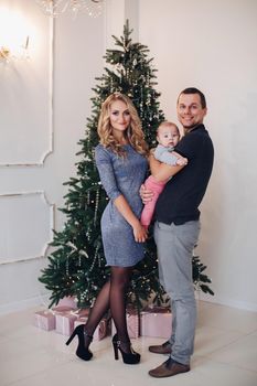 New Year concept photo of a happy young family of two parents and a baby posing near Christmas tree