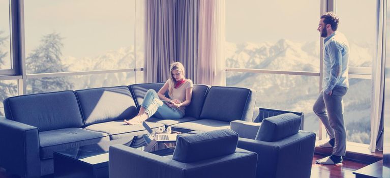 Young couple relaxing at  home using tablet computer reading in the living room near the window on the sofa couch.