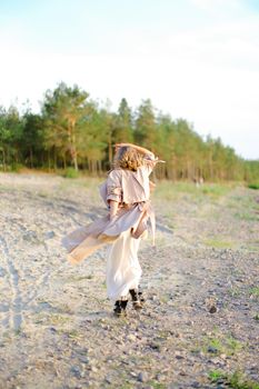 Young blonde woman turning around on sand and wearing coat with white dress. Concept of happiness, summer vacations and fashion.