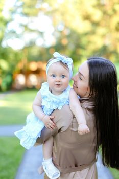 Back view of brunette mother holding little daughter in garden. Concept of motherhood and resting on open air.