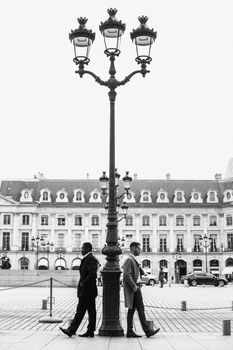 Black and white photo of afro american and caucasian boys standing near street lantern, wearing suits. Concept of urban photo session and life style.