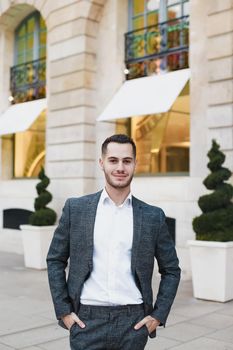 Young cacuasian male person wearing suit standing near building outdoors. Concept of fashion and businessman, urban life.