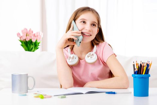 Adorable girl making calls to her school friends in free time