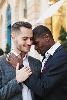 Afro american gay hugging caucasian boy outside, wearing suits. Concept of lgbt and same sex couple.