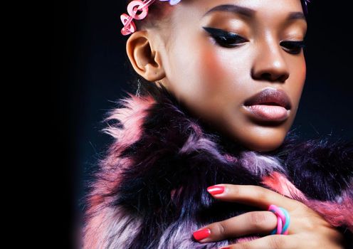 young pretty african american woman in spotted fur coat and flowers on head smiling on black background, fashion people concept close up