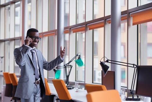 Happy smiling successful African American businessman  in a suit in a modern bright office indoors speel on phone