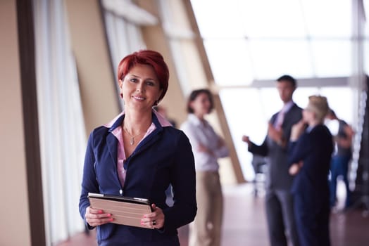 Smilling young business woman with tablet computer  in front her team blured in background. Group of young business people. Modern bright  startup office interior.