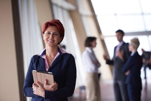 Smilling young business woman with tablet computer  in front her team blured in background. Group of young business people. Modern bright  startup office interior.