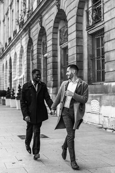 Black and white bw portrait in Paris. Caucasian man running with afroamerican male person and holding hands in city. Concept of happy gays and strolling.