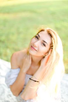 Portrait of young european woman sitting on plaid, grass in background. Concept of beautiful female person and summer season.