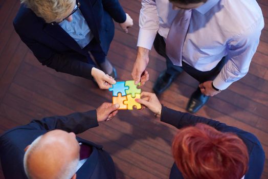 business people group assembling jigsaw puzzle and represent team support and help concept, top view perspective at modern bright office interior