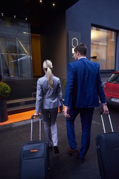 Young business people couple entering city  hotel, looking for room, holding suitcases while walking on street