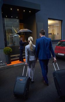 Young business people couple entering city  hotel, looking for room, holding suitcases while walking on street