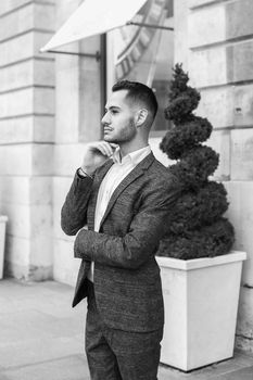 Black and white bw portrait in Paris. Young cacuasian male person wearing suit and wite shirt standing near building outdoors. Concept of fashion and businessman, urban life.