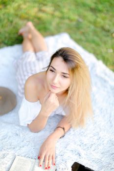 Young girl with red nails lying on plaid in park and reading book. Concept of having free time, resring and picnic.