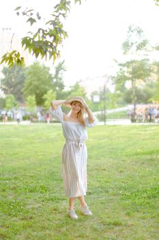 Young g caucasian girl wearing hat and dress, standing in park on grass. Concept of summer season fashion and female person.