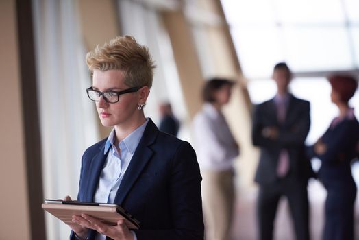 Smilling young business woman with tablet computer  in front her team blured in background. Group of young business people. Modern bright  startup office interior.