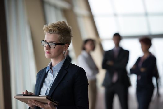 Smilling young business woman with tablet computer  in front her team blured in background. Group of young business people at modern bright  startup office interior.