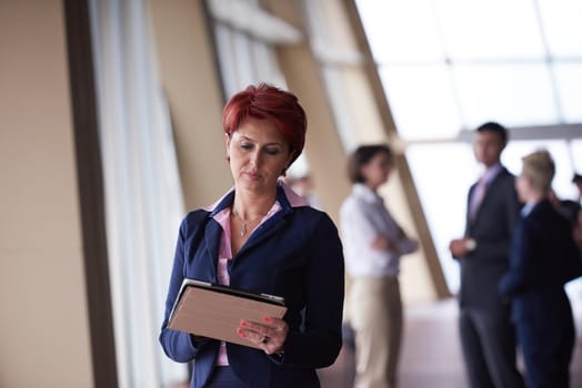 Smilling young business woman with tablet computer  in front her team blured in background. Group of young business people. Modern bright  startup office interior.