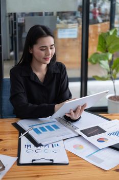 Attractive businesswoman using a digital tablet while working with paperwork financial data chart on wooden desk