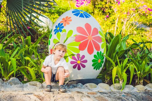 Cute little kid boy with bunny ears having fun with traditional Easter eggs hunt, outdoors. Celebrating Easter holiday. Toddler finding, colorful eggs.