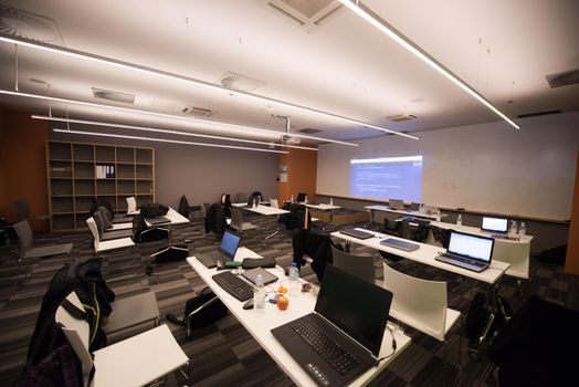 empty it classroom with program code on projector screen and modern laptop computers on table