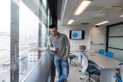 relaxed young businessman using smart phone at modern startup business office meeting room  with big window and city in backgronud