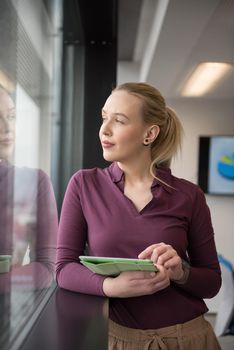 Blonde businesswoman in casual  clothes working on tablet computer at modern startup business office interior. Young people group on team meeting blured  in background