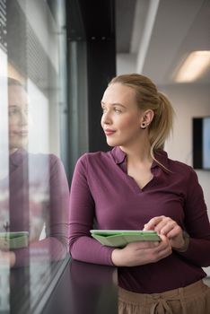 Blonde businesswoman in casual  clothes working on tablet computer at modern startup business office interior. Young people group on team meeting blured  in background