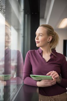 Blonde businesswoman in casual  clothes working on tablet computer at modern startup business office interior. Young people group on team meeting blured  in background