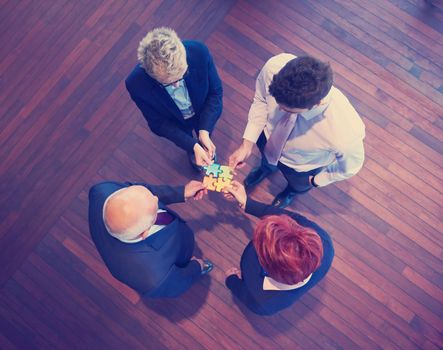 business people group assembling jigsaw puzzle and represent team support and help concept, top view perspective at modern bright office interior