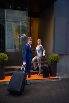 Young business people couple entering city  hotel, looking for room, holding suitcases while walking on street