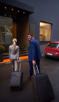 Young business people couple entering city  hotel, looking for room, holding suitcases while walking on street