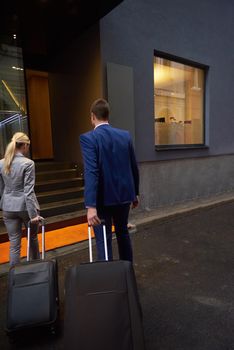 Young business people couple entering city  hotel, looking for room, holding suitcases while walking on street